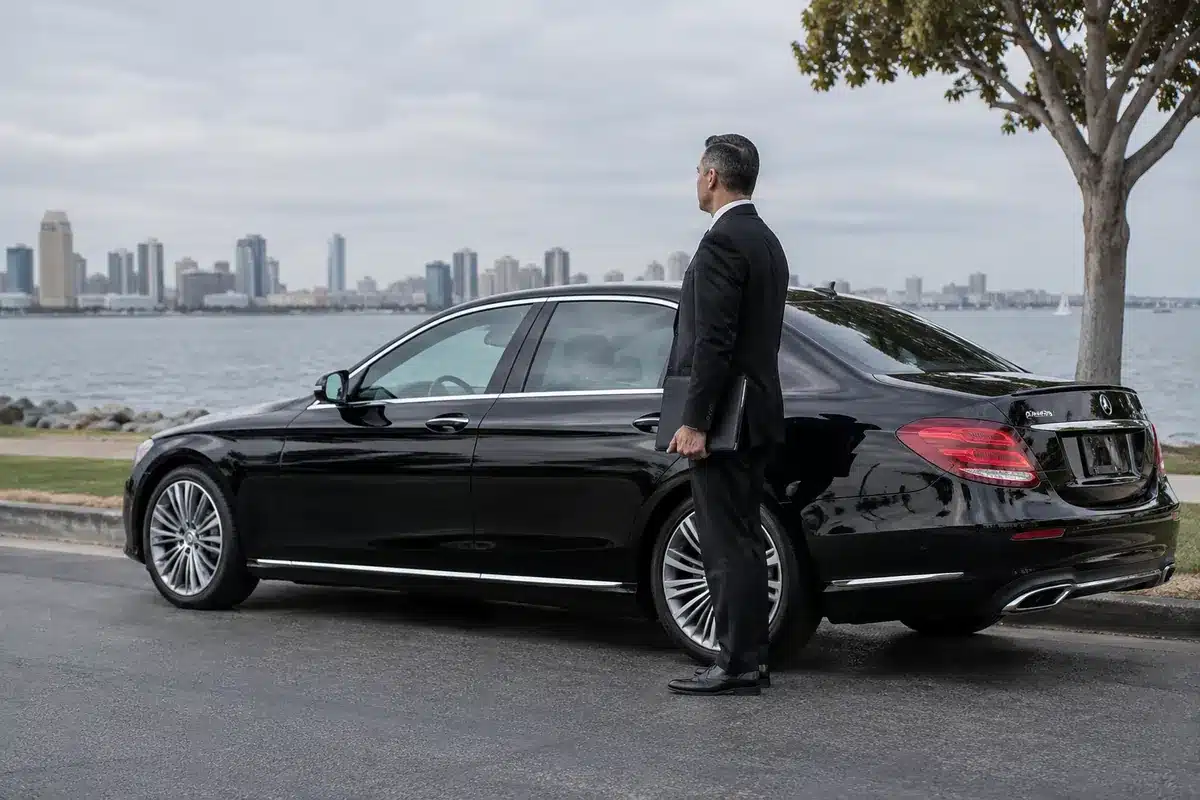 Chauffeur beside a black sedan at the San Diego waterfront.